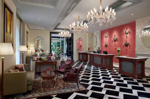 Un vestíbulo lujoso con piso a cuadros, muebles elegantes, candelabros y espejos decorativos.