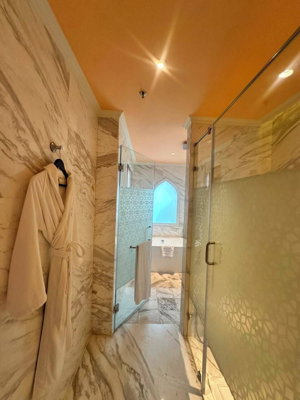 A bathroom with marble walls, a glass shower enclosure, and a robe hanging on a rack.