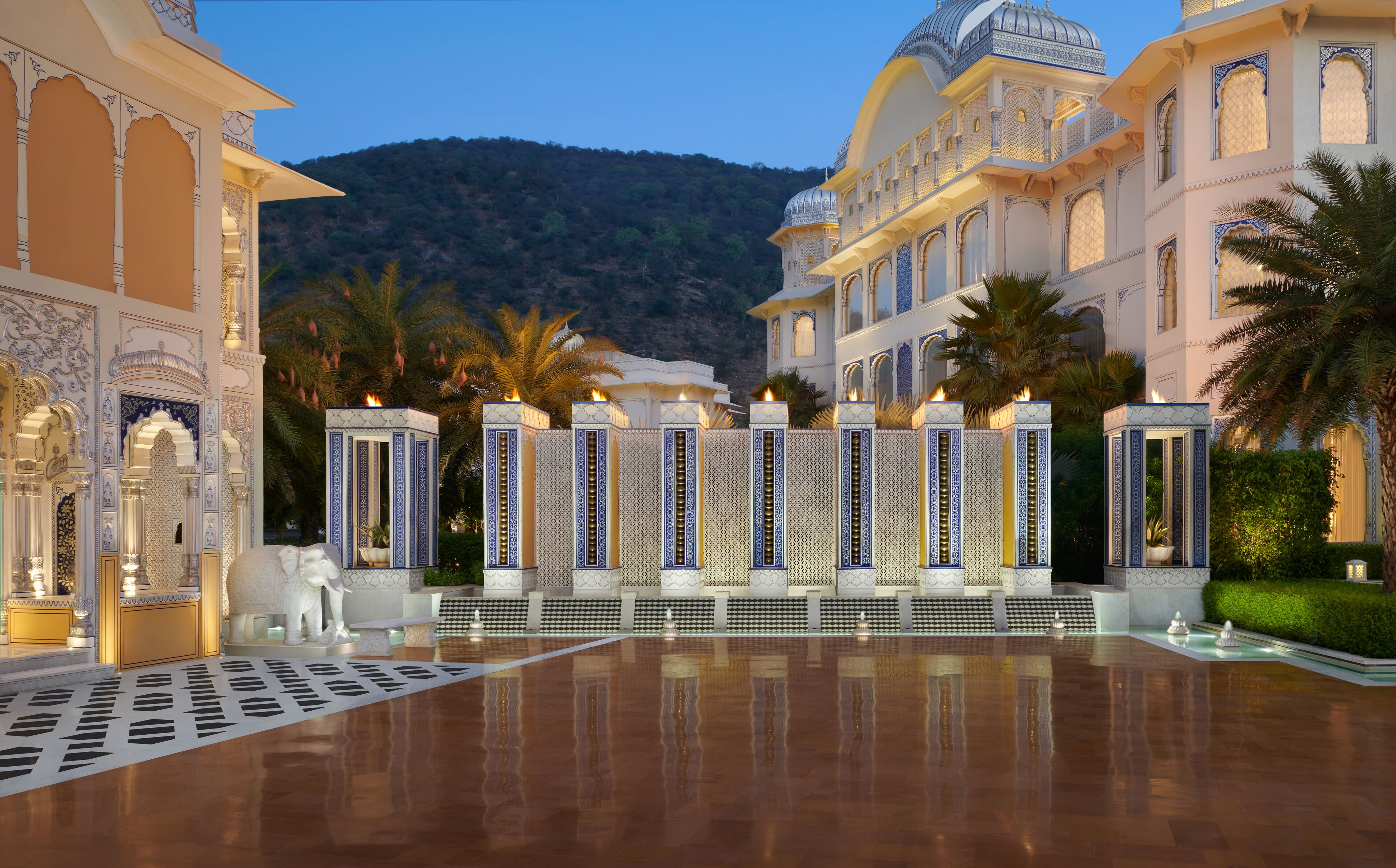 A grand hotel courtyard with ornate columns, a reflective pool, and a mountainous backdrop.
