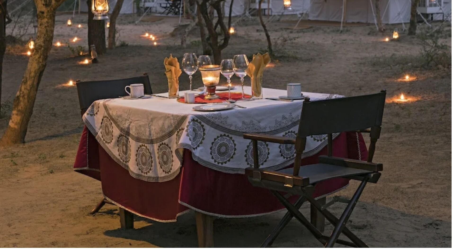 Une table de salle à manger ronde, installée à l’extérieur, avec une nappe, des chaises et des bougies.