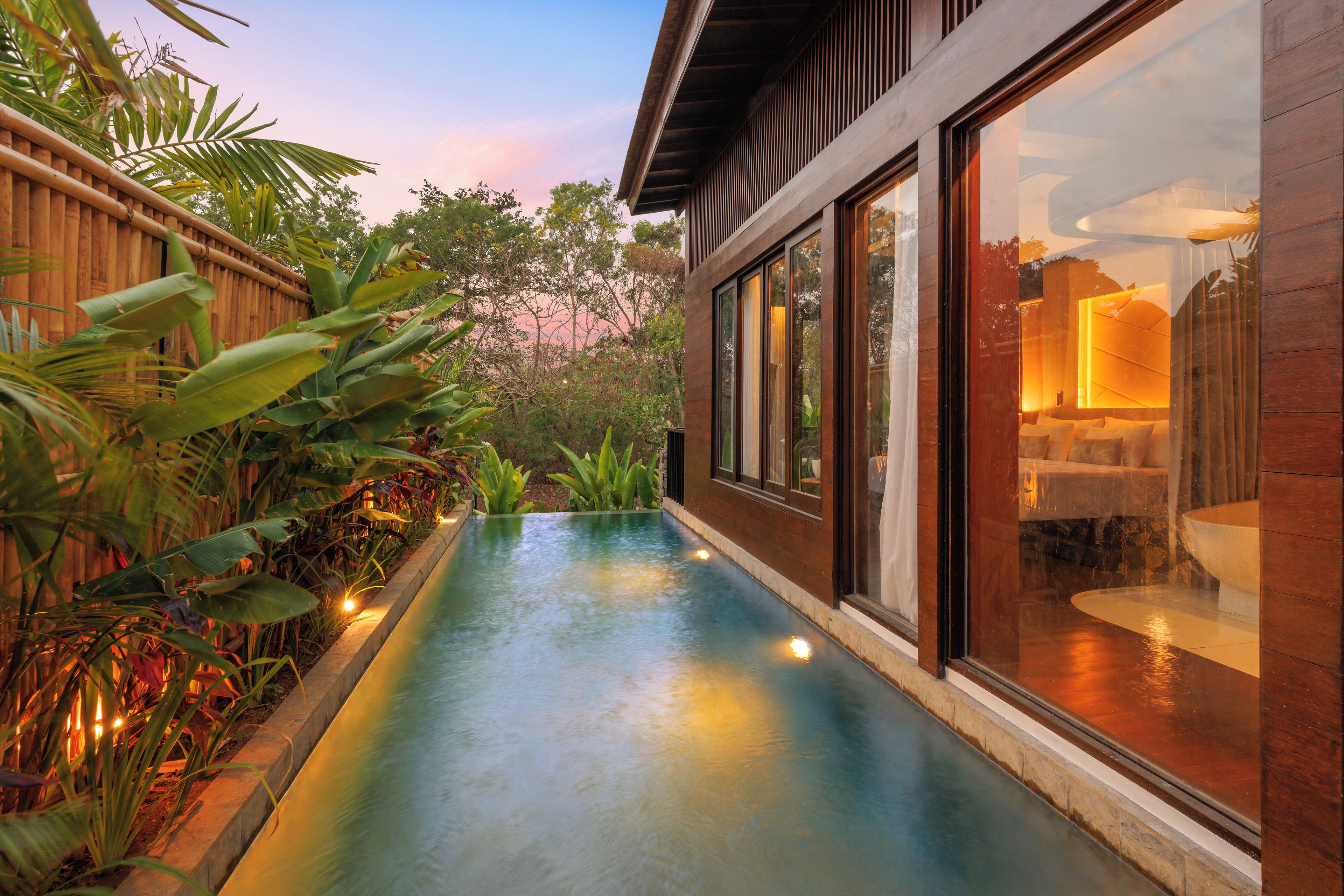 A modern building with a glass facade, a pool, and lush tropical plants.