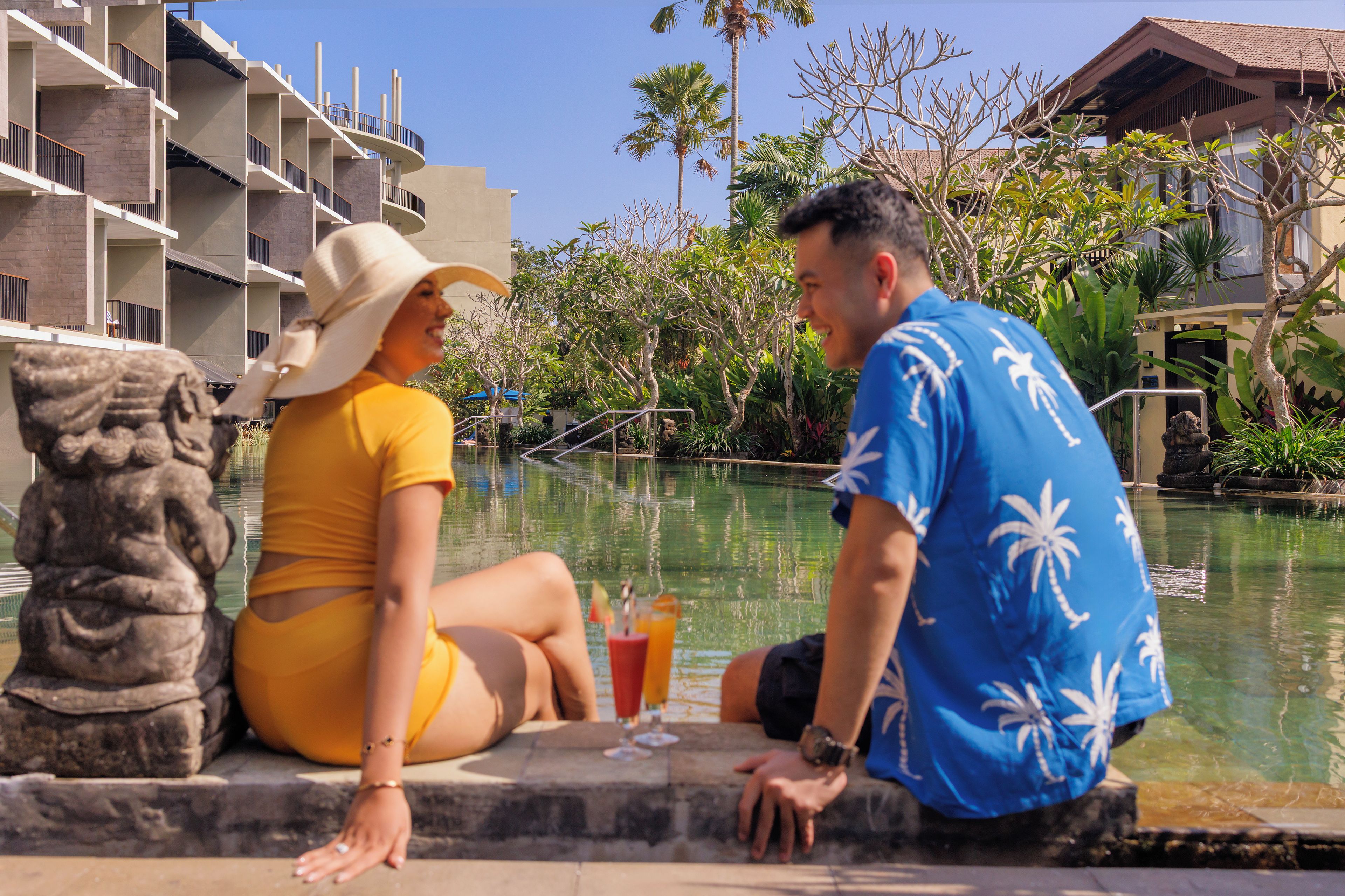 A couple sitting by a pool with a modern building in the background.