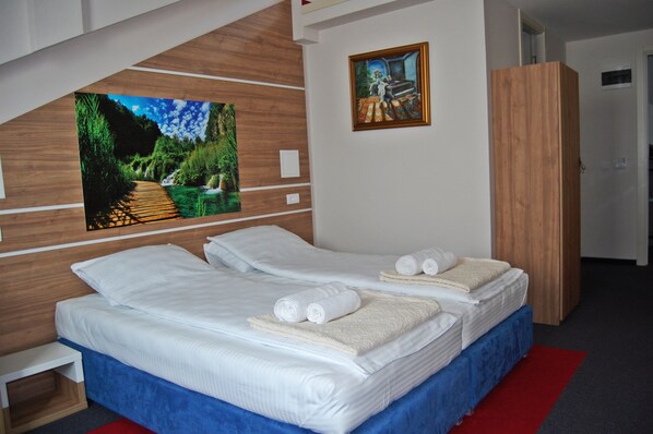 Cama doble con ropa de cama y toallas blancas, cabecera de madera, alfombra roja y un cuadro de un paisaje en la pared.
