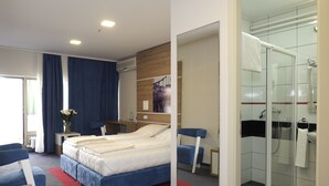 A modern hotel room with a bed, a desk, a chair, a shower area, and a large mirror. - Guest House Vida (Belgrade)