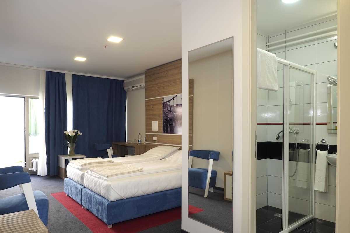 Une chambre d’hôtel moderne équipée d’un lit, d’un bureau, d’une chaise, d’un espace douche et d’un grand miroir.
