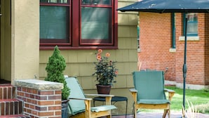 A patio with a brick fireplace, a wooden bench, and a green chair. There is a potted plant and a small tree on the patio. - 1936 Keystone Cottage - Family Friendly (Boise)
