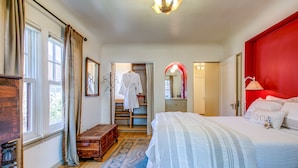 A bedroom with a bed, a wooden chest, a wardrobe, a mirror, and a red accent wall. - 1936 Keystone Cottage - Family Friendly (Boise)