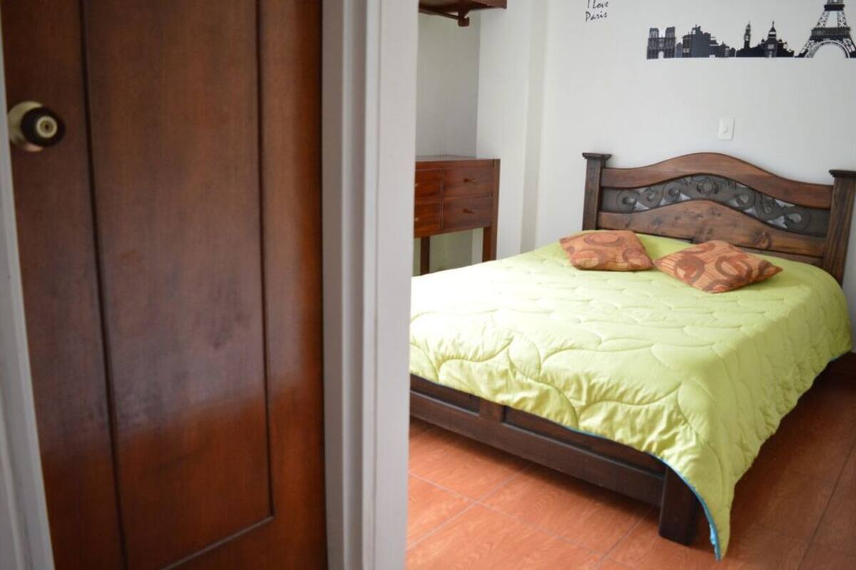 A bedroom with a wooden bed, a green bedspread, and a wall decoration of Paris landmarks.