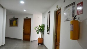 A hallway with a fire extinguisher, a plant, and a door with an exit sign. - Hotel Dancar (Pamplona)