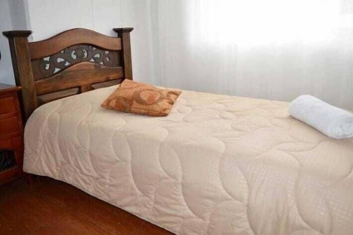 A bed with a wooden headboard, a beige quilted bedspread, a brown pillow, and a rolled white towel.