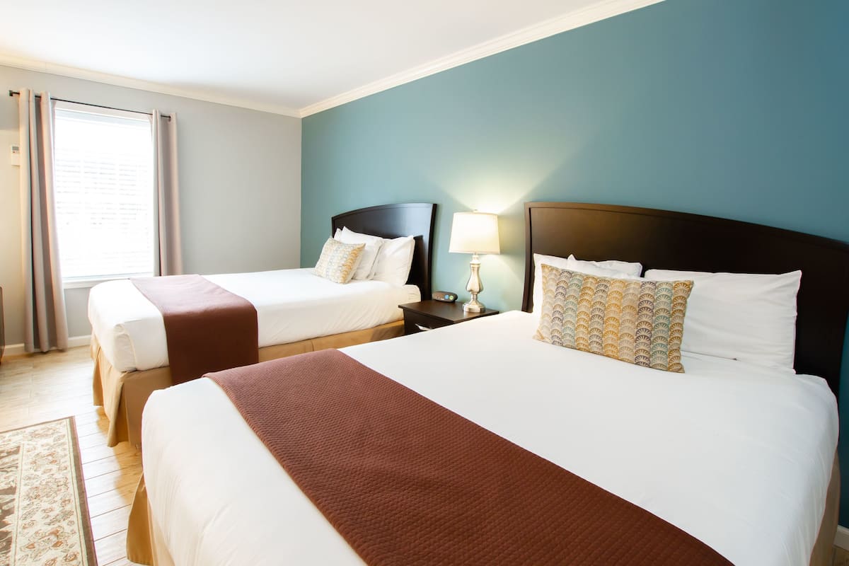 A hotel room with two beds, a nightstand with a lamp, and a window with curtains.