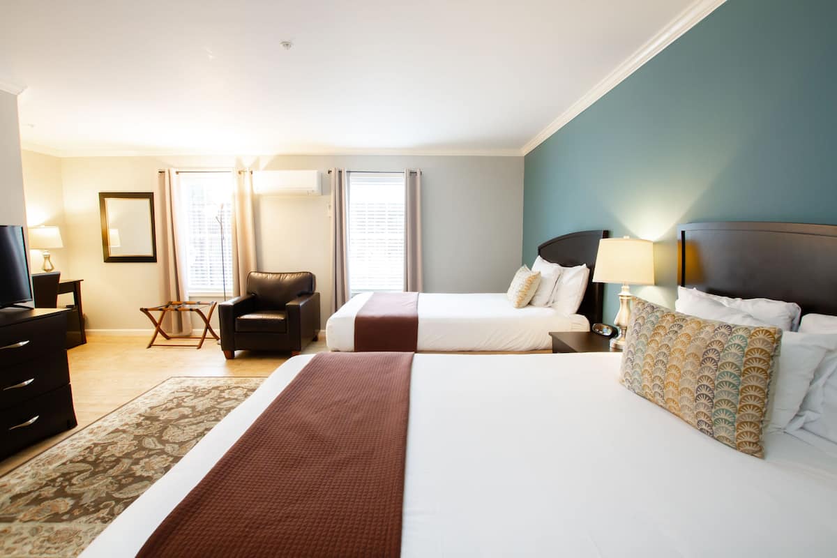 A hotel room with a large bed, a smaller bed, a desk, a chair, and a TV.