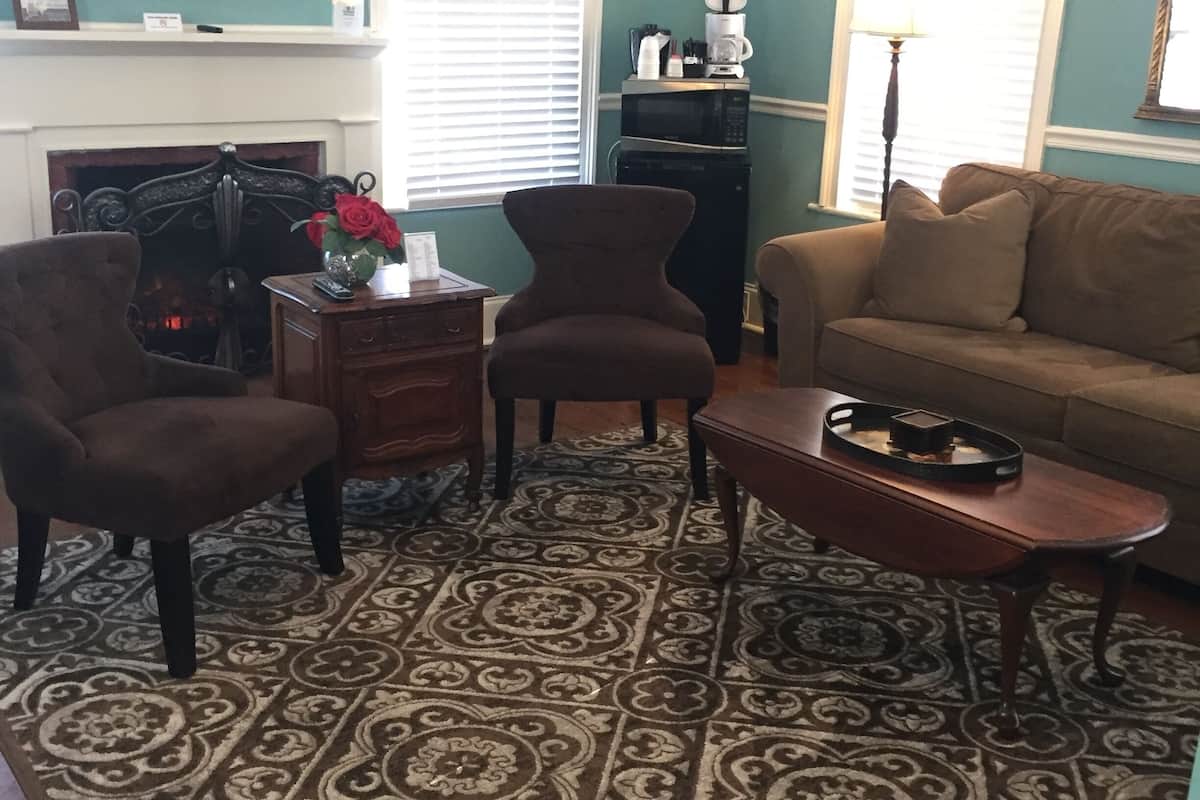 A living room with a patterned carpet, a sofa, two armchairs, a coffee table, a fireplace, and a painting on the wall.