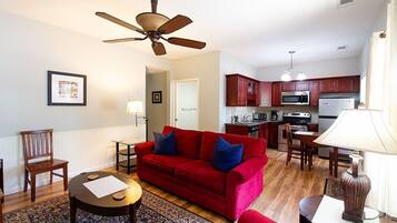 A compact living space with a red sofa, a dining table, a kitchen area with wooden cabinets, and a ceiling fan.