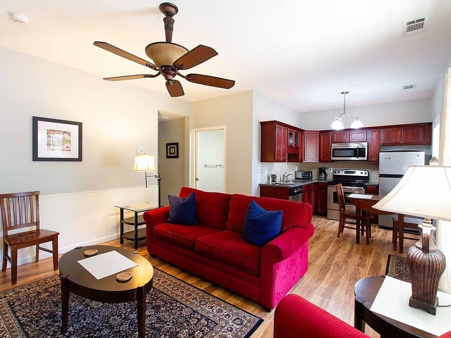 A compact living space with a red sofa, a dining table, a kitchen area with wooden cabinets, and a ceiling fan.