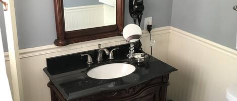 Un baño con tocador de madera oscura, un lavabo blanco y un espejo grande arriba.