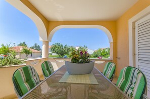 A covered patio with a table and chairs, a large planter with flowers, and a view of the neighborhood. - Apartments Biserka (Novalja)