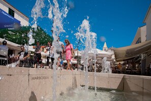 A public fountain with water jets, surrounded by people and outdoor seating areas. - Apartments Biserka (Novalja)