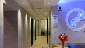 A hotel corridor with a reception desk, a large illuminated logo, and a potted plant. - Buonarroti Suite (Rome)