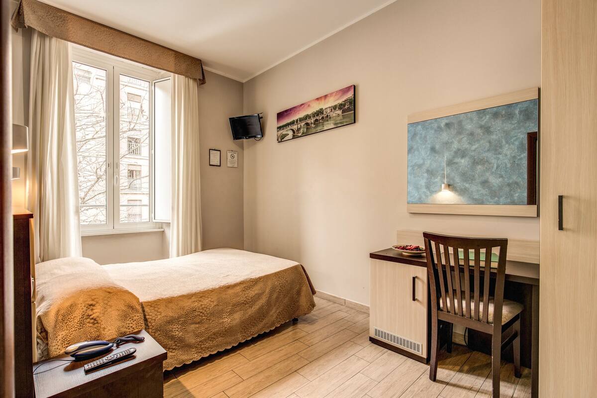 A bedroom with a bed, a desk, a chair, a TV, and a painting on the wall.