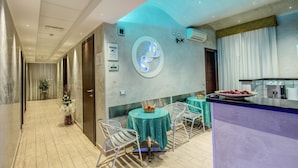 A modern hotel lobby with a reception desk, a dining area with round tables, and a kitchen area. - Buonarroti Suite (Rome)