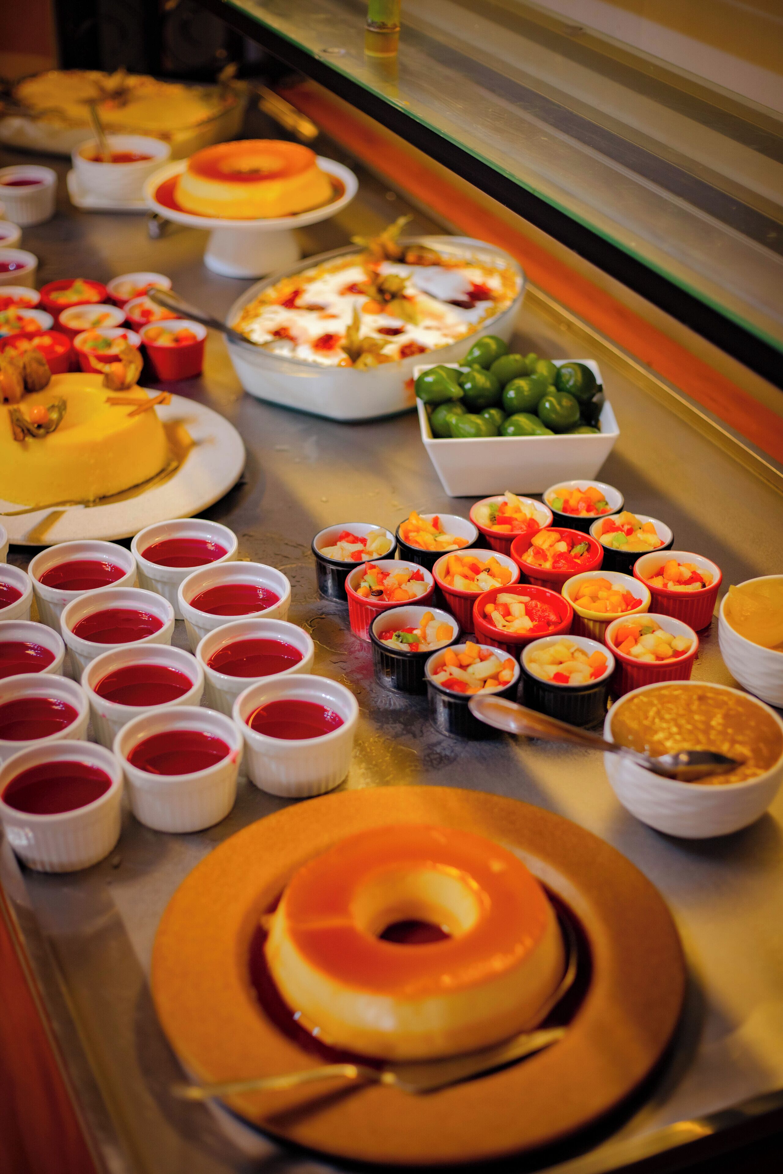 Un bufé con diversos platos, incluyendo un pastel amarillo grande, varios vasos rojos pequeños y un tazón de limas verdes.