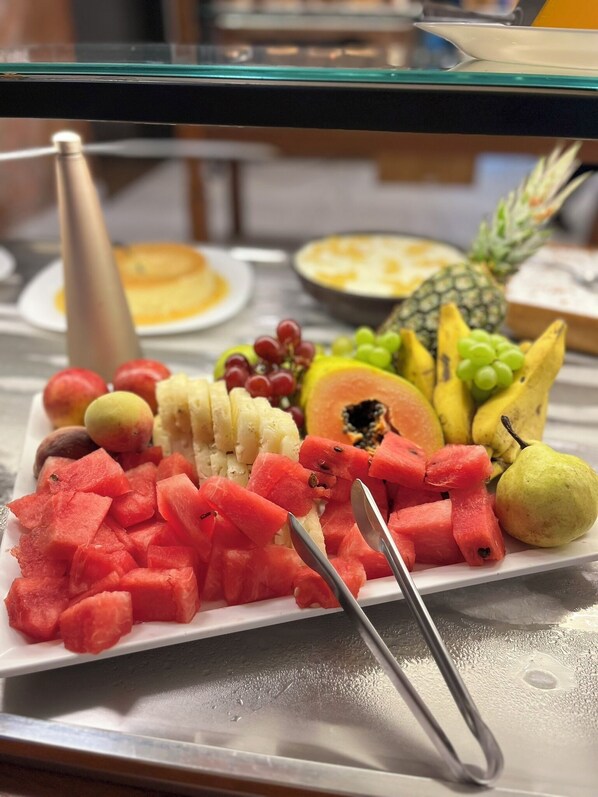 A fruit platter with watermelon, grapes, pineapple, and bananas on a white plate.