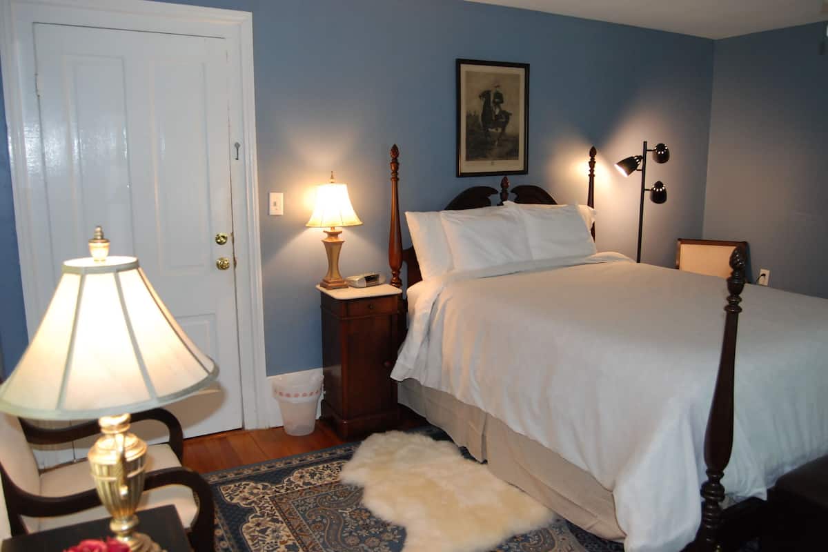 A bedroom with a bed, a nightstand, a lamp, a door, and a framed picture on the wall.