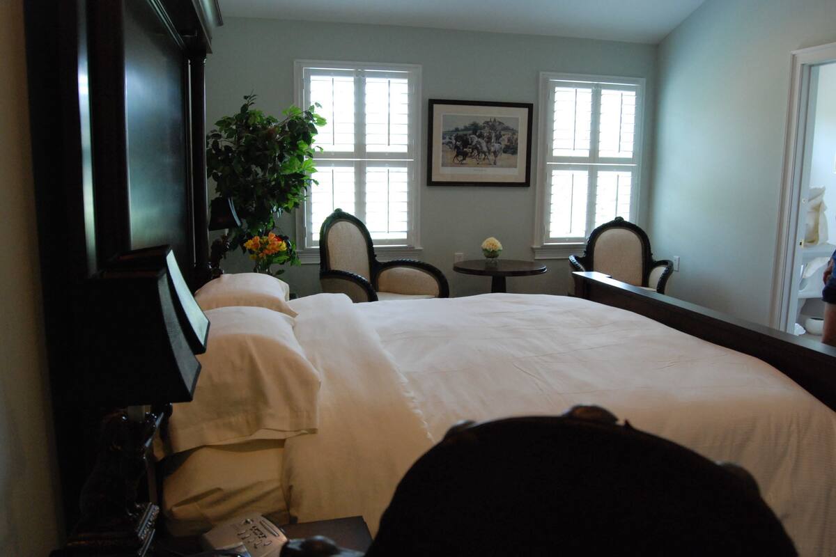 A hotel room with a large bed, two chairs, a small table with a vase, and a framed picture on the wall.