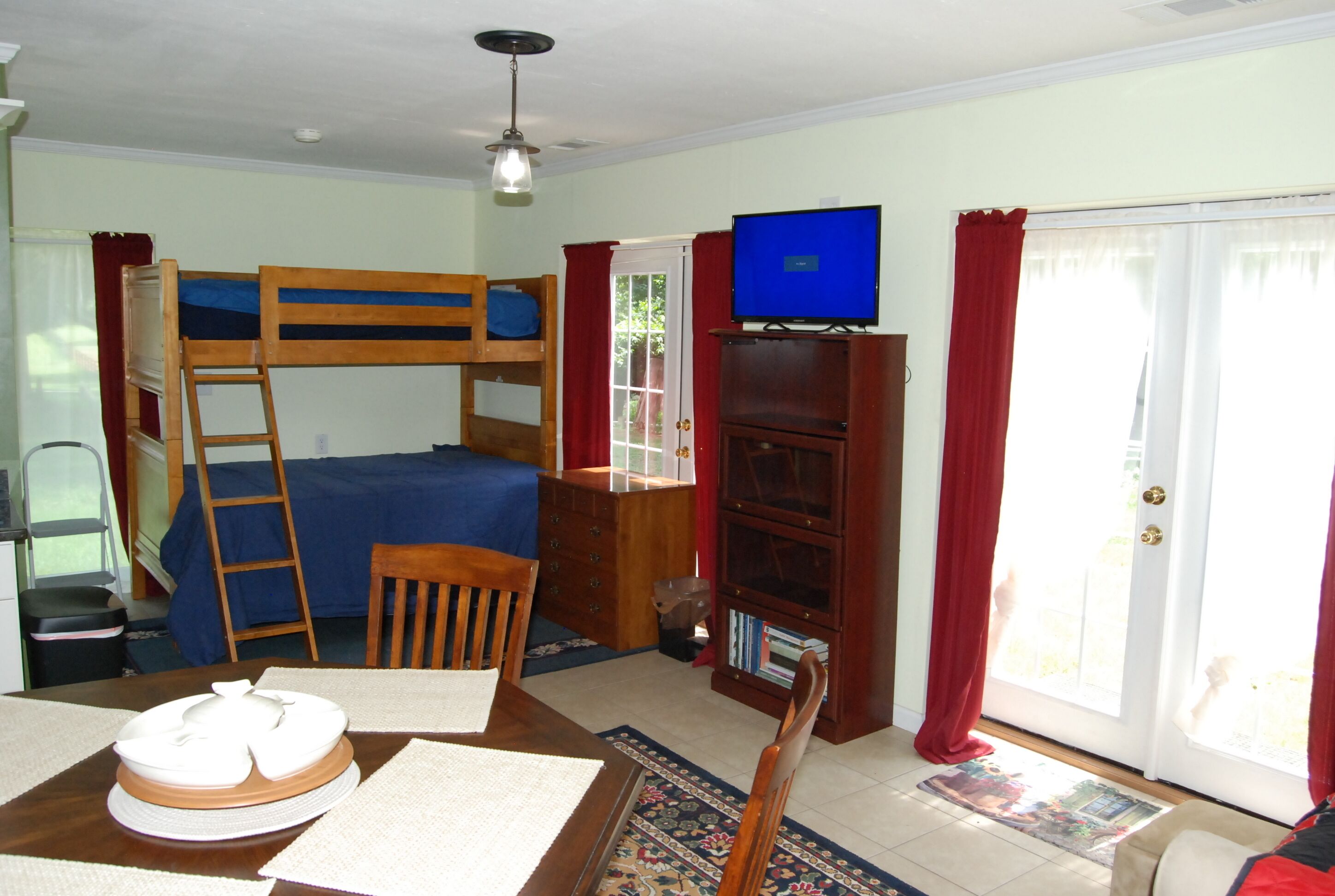A room with a bunk bed, a desk with a computer, a television, and a bookshelf.