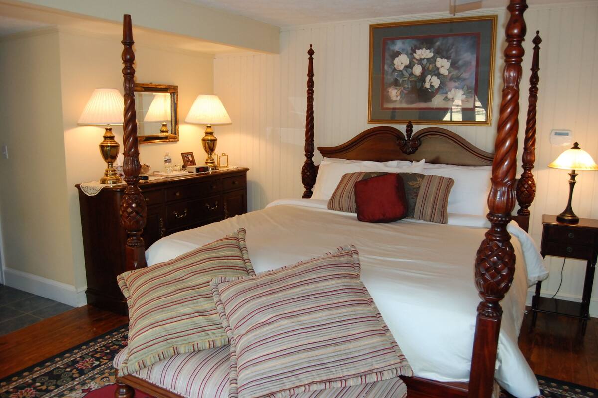 A four-poster bed with a wooden headboard, a dresser with a mirror, and two bedside lamps.