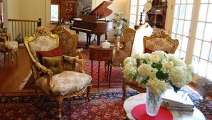A grand room with a grand piano, ornate chairs, a red patterned rug, and a vase of flowers. - The Colonels B&B and Inn (Athens)
