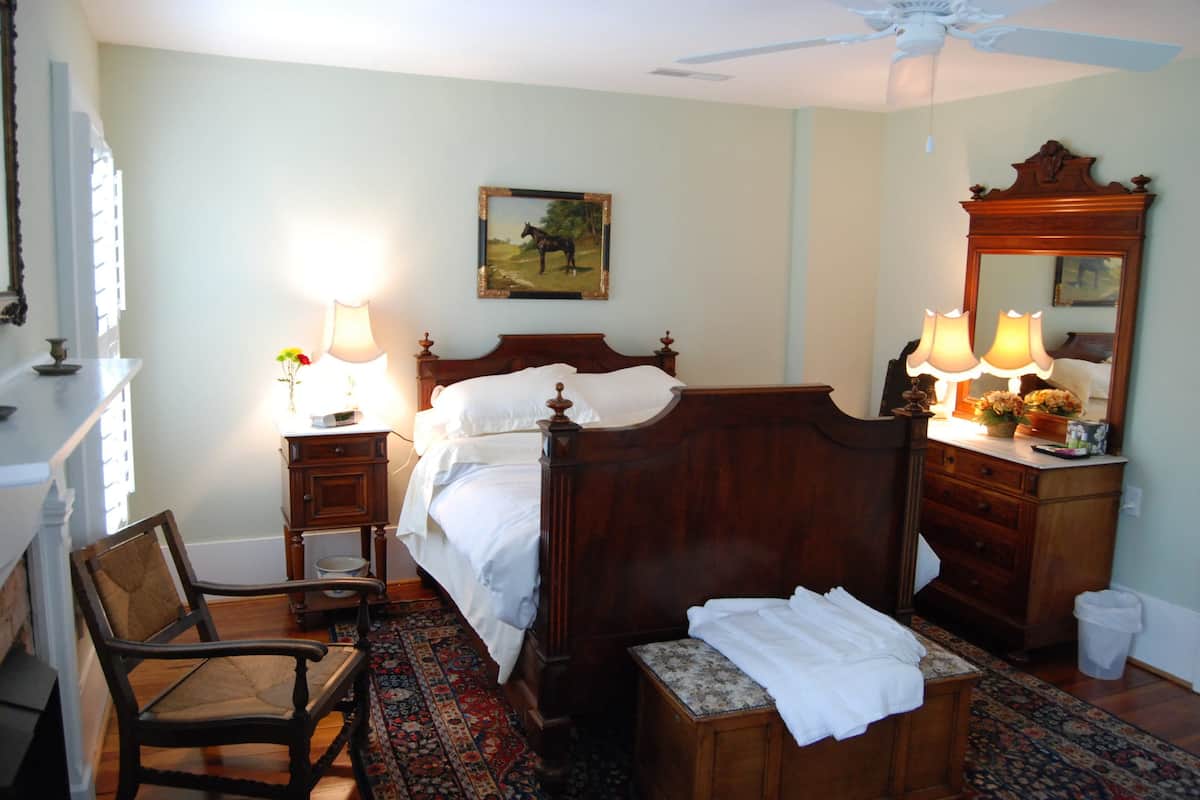 A bedroom with a wooden bed, two bedside tables with lamps, a chair, a dresser, and a mirror.