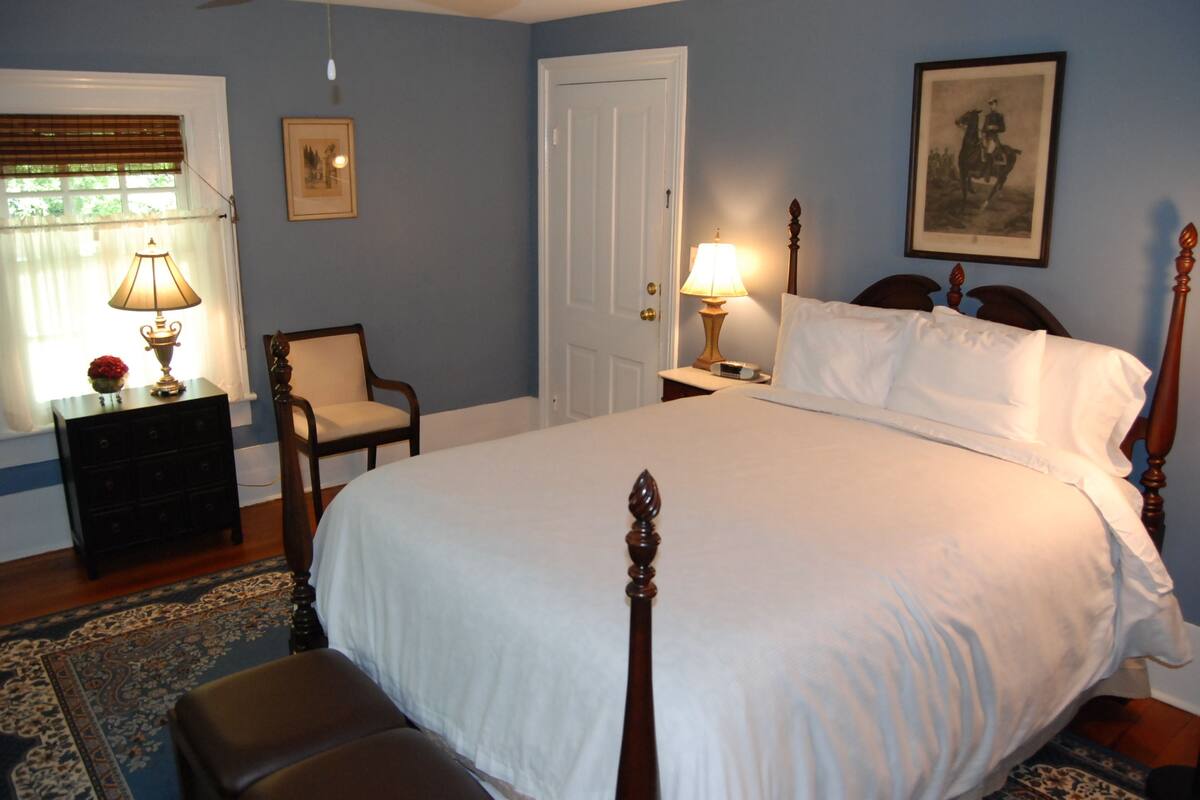 A bedroom with a large bed, a chair, a dresser, and a door.