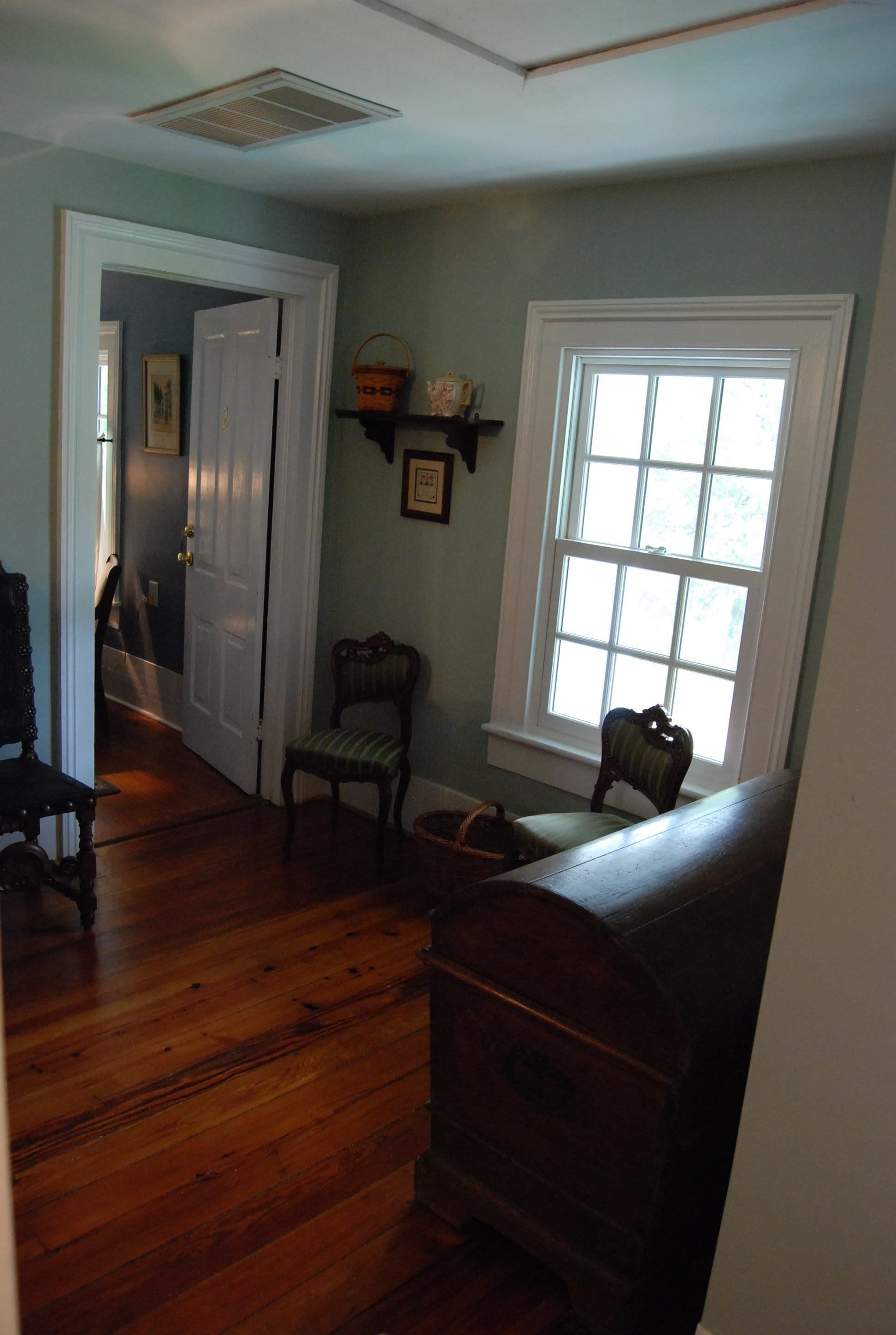 A room with hardwood floors, a chair, a bench, a window, and a door leading to another room.