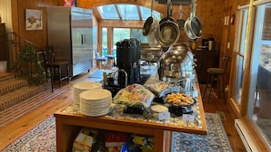 A kitchen with wooden walls, a central island with food items, hanging pots, and a refrigerator. - The Colonels B&B and Inn (Athens)