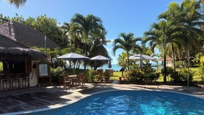 A pool area with a bar, umbrellas, and a view of the ocean. - Etu Moana Boutique Beach Villas - Adults Only (Aitutaki)