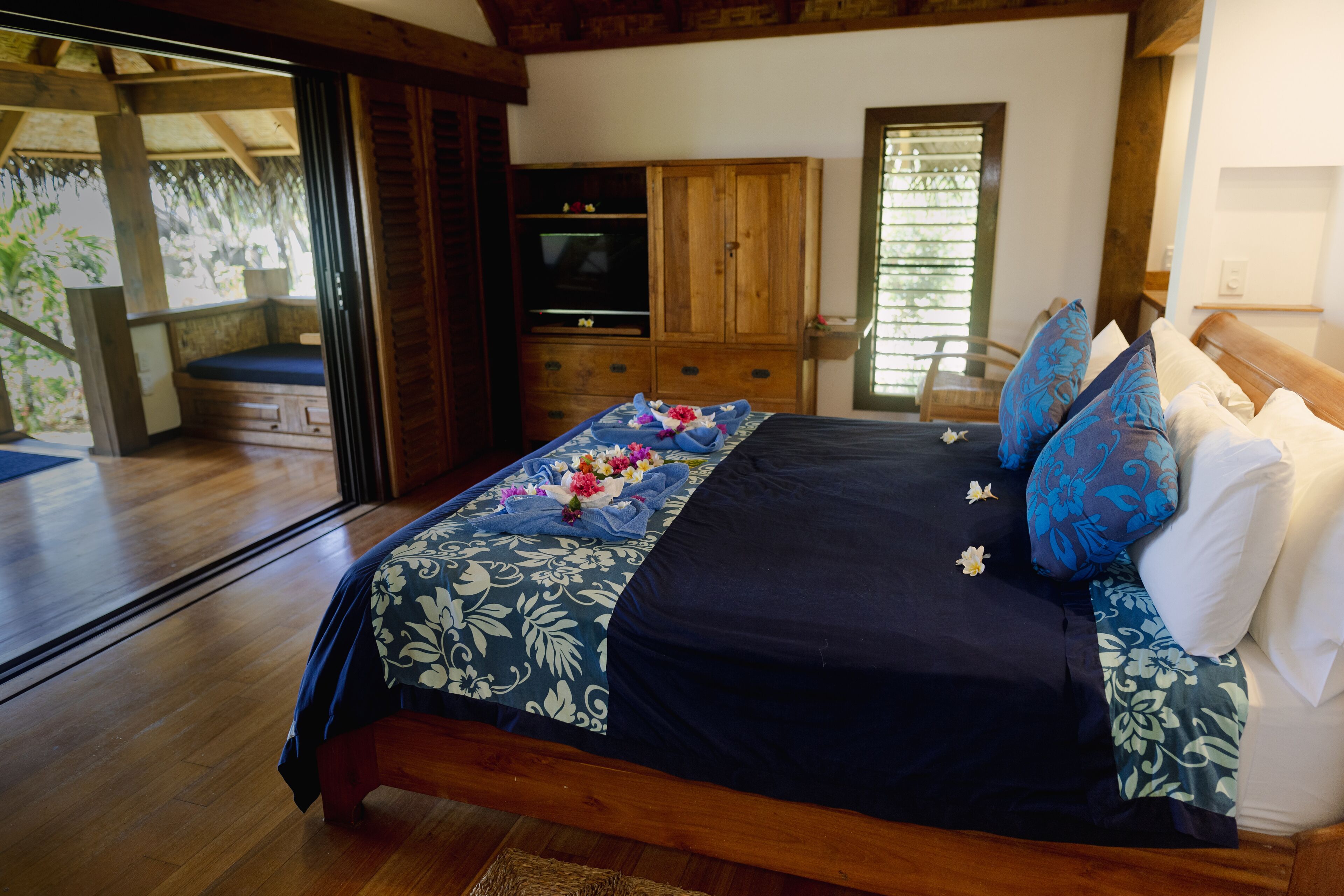 Un dormitorio con cama de madera, televisor y puerta corrediza de vidrio que da a un espacio exterior.