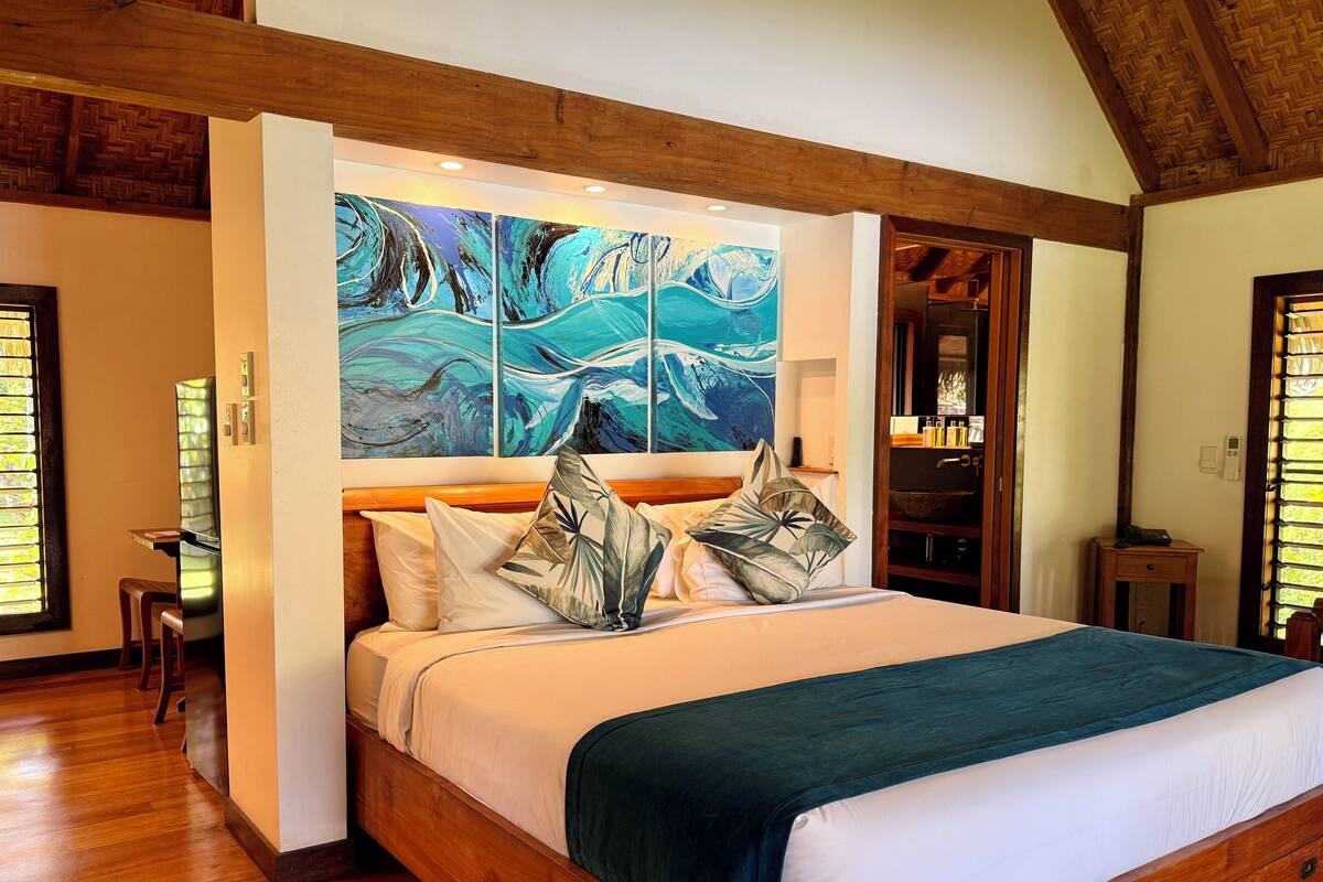 A bedroom with a wooden bed, a large abstract painting, and a wooden ceiling.