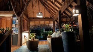 A cozy, well-lit interior with a wooden ceiling, a large potted plant, and a wicker chair. - Etu Moana Boutique Beach Villas - Adults Only (Aitutaki)