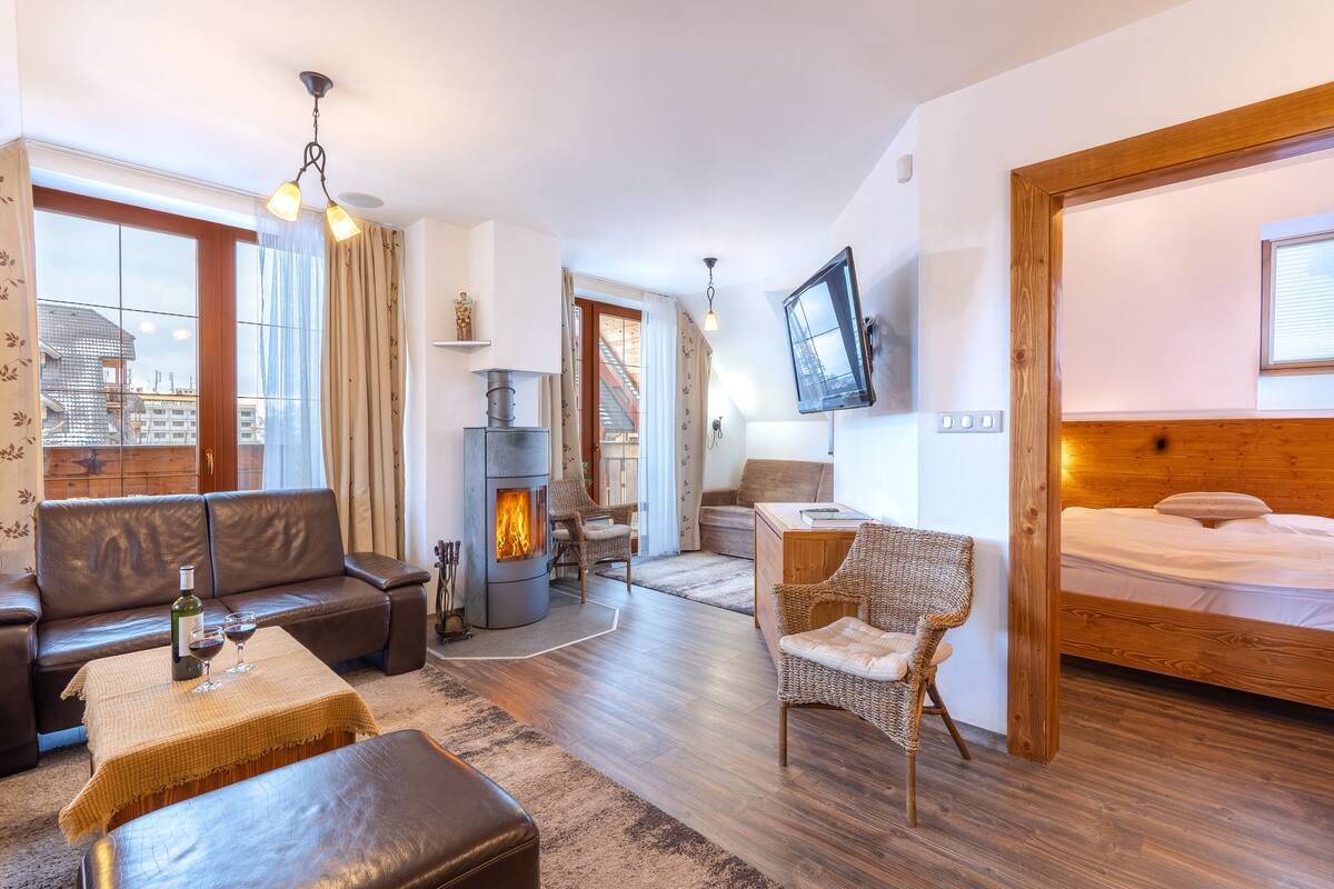 Een gezellige woonkamer met een open haard, leren bank en een eethoek met een houten tafel en stoelen.