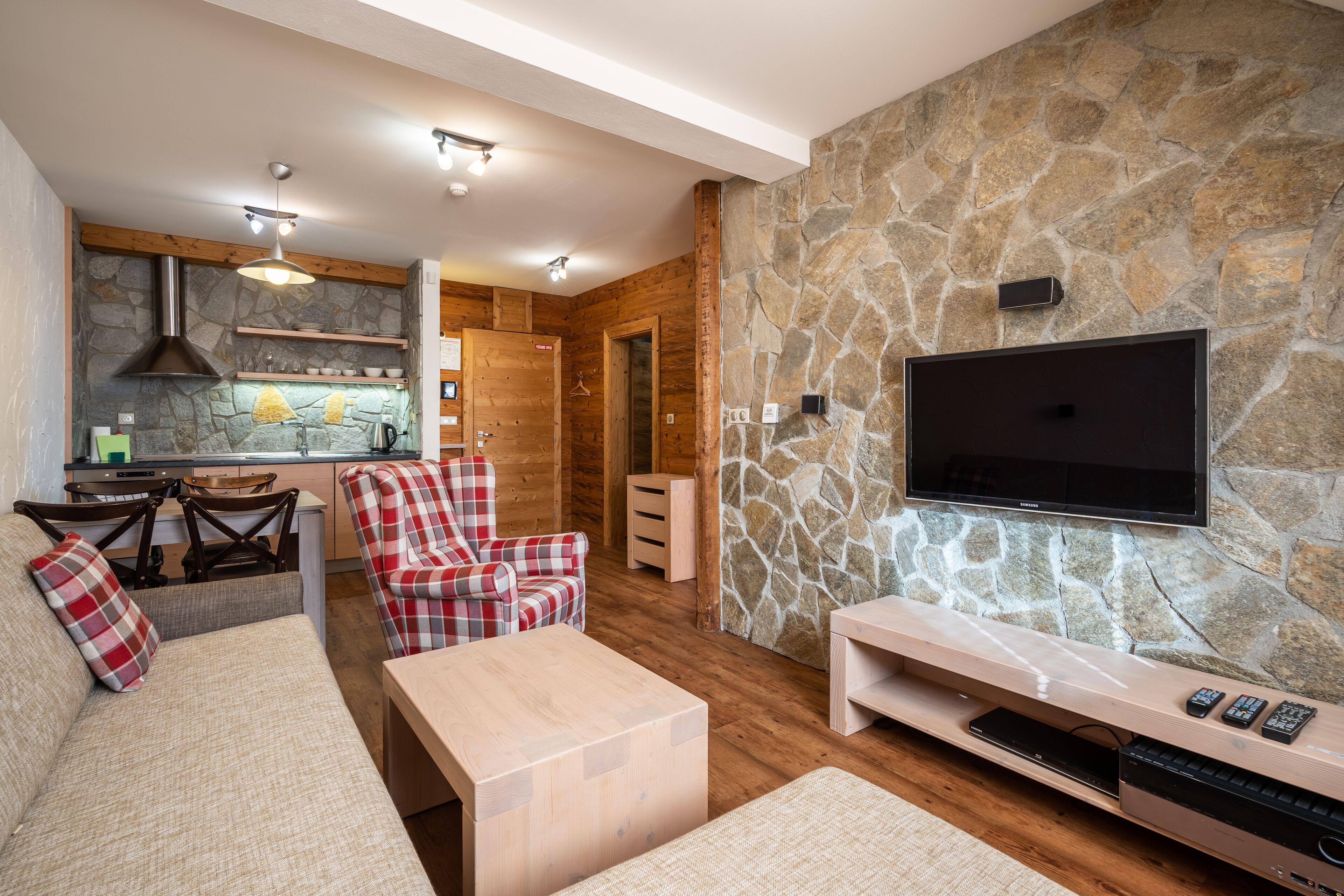 A cozy living room with a stone wall, a flat-screen TV, a wooden coffee table, and a plaid armchair.