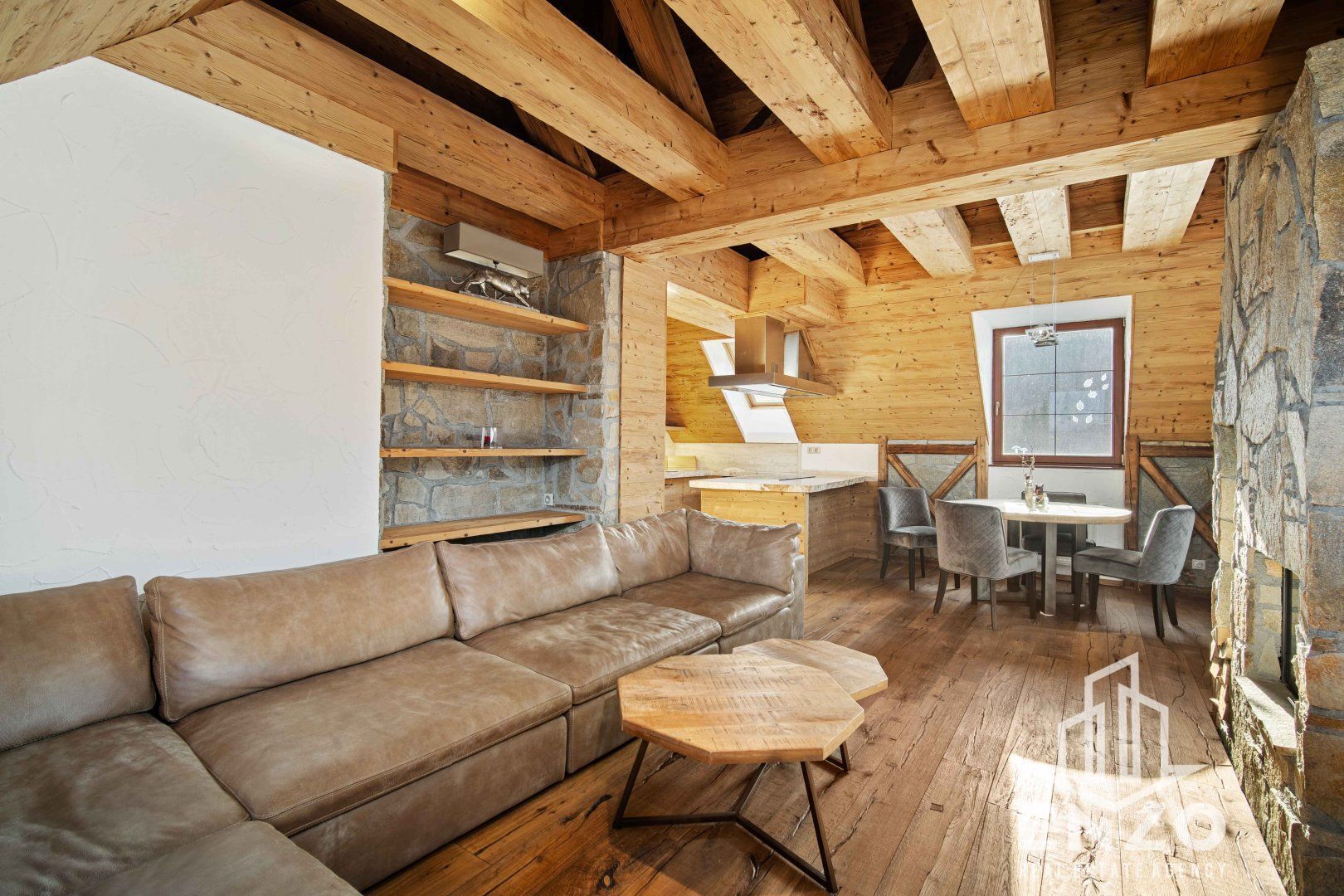 Un interior de cabaña acogedor con techo de madera, paredes de piedra, un sofá de cuero, una mesa de comedor con sillas y una chimenea de piedra.