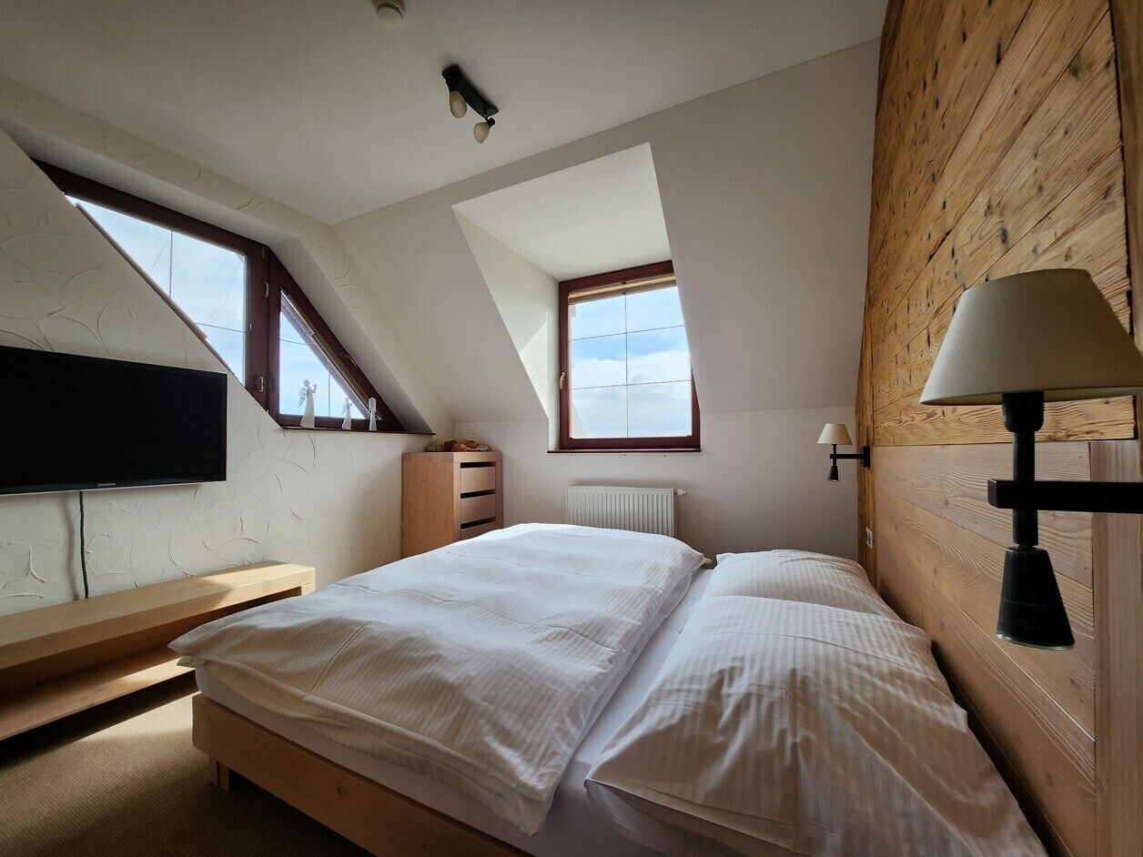 Une chambre avec un plafond en pente, un lit, un bureau, une télévision et une fenêtre donnant sur un beau paysage.