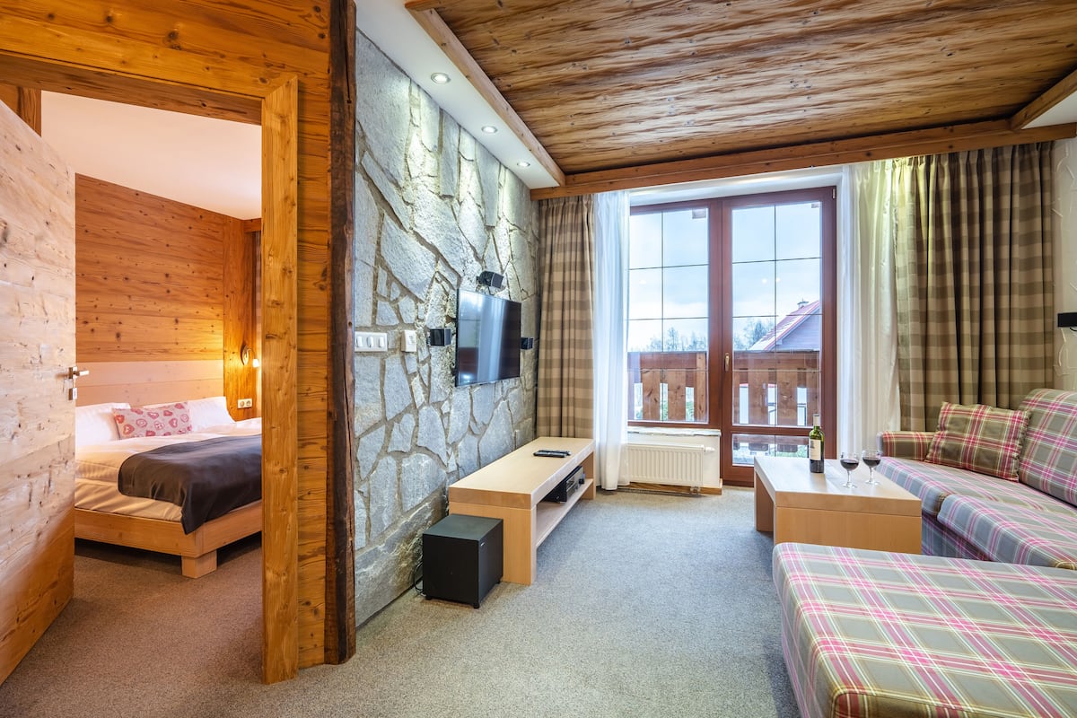 Een knus ingerichte kamer met een bed, een bank, een televisie bevestigd aan een stenen muur en een raam met gordijnen.