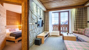 A cozy room with a bed, a sofa, a TV mounted on a stone wall, and a window with curtains.