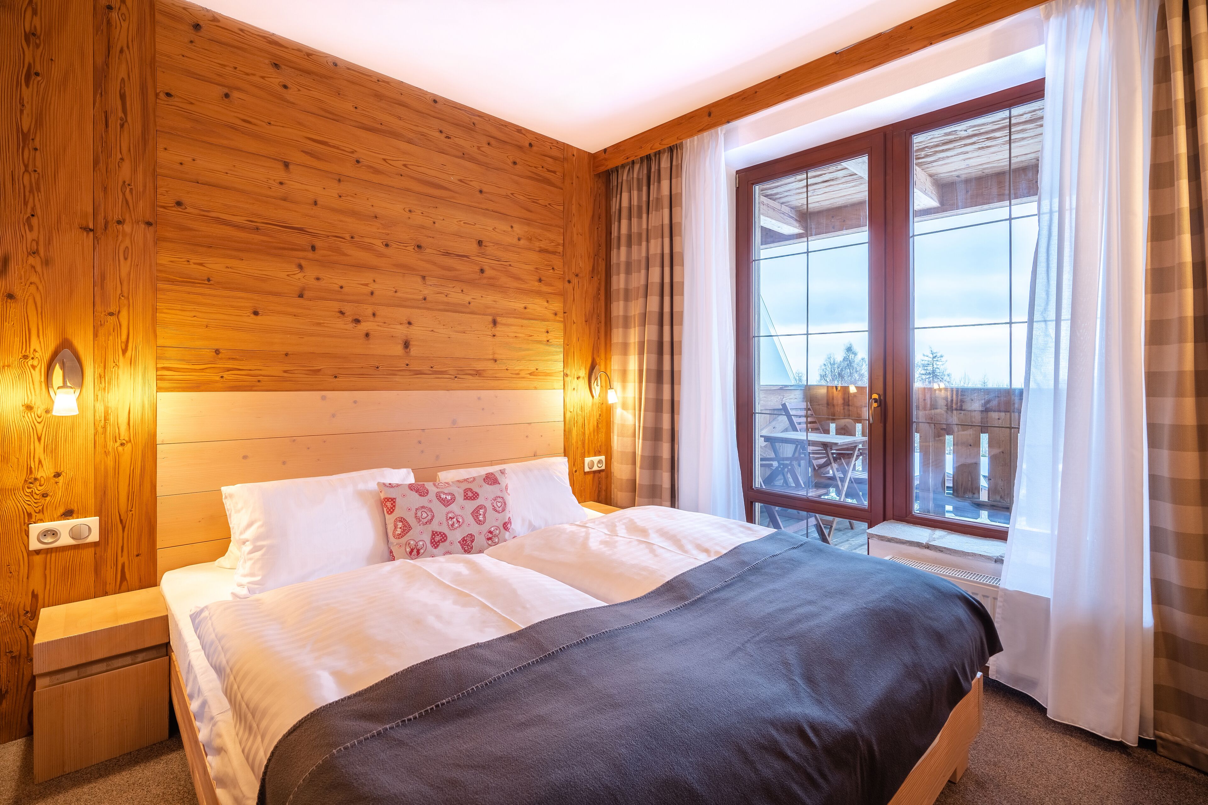 A wooden-paneled bedroom with a large bed, a nightstand, and a window with curtains.