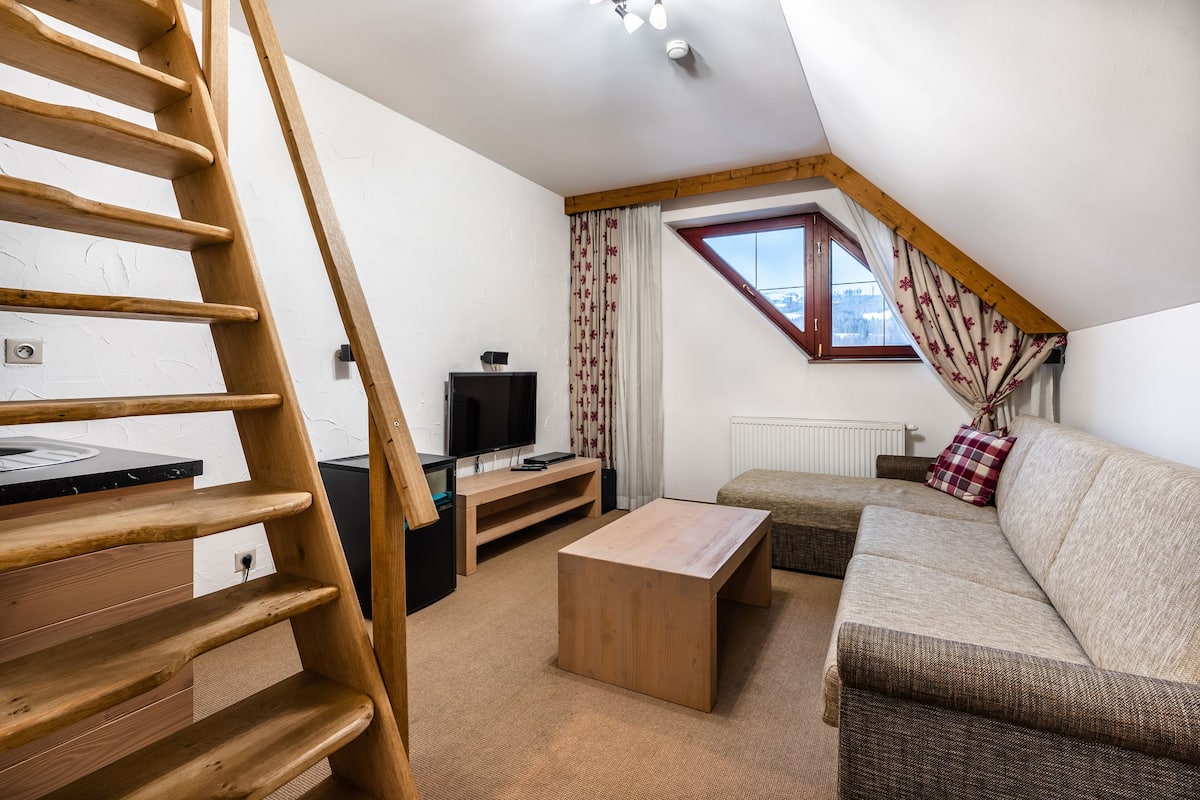 Een loftachtige kamer met een houten trap, een bank, een salontafel en een televisie.