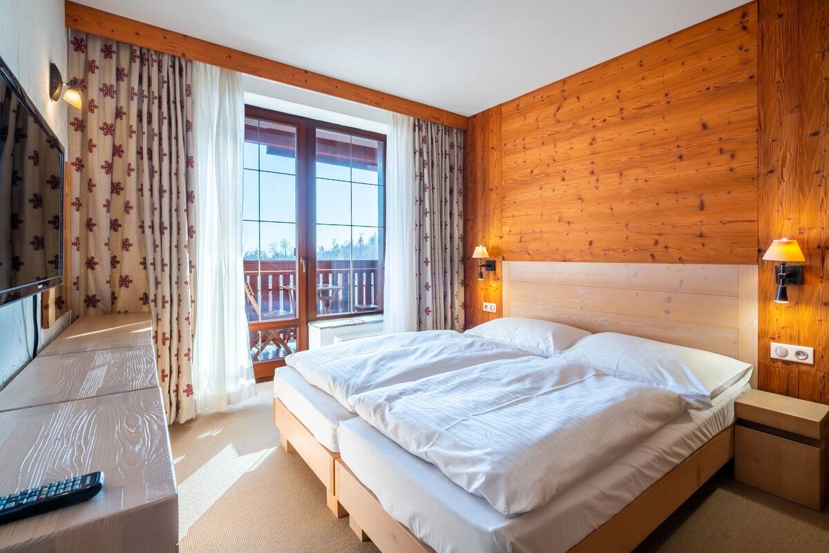 Een slaapkamer met een houten hoofdbord, een bed met witte lakens, een nachtkastje met een lamp en een raam met gordijnen.