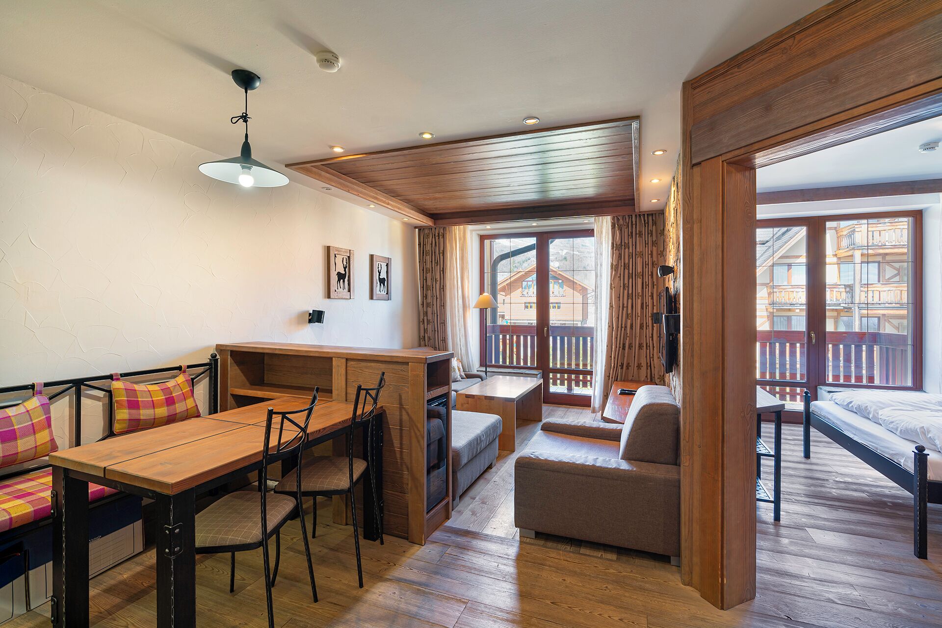 A cozy room with a wooden dining table, chairs, a sofa, and a balcony with wooden railings.
